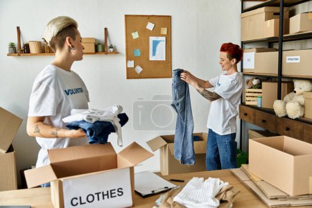 Un jeune couple de lesbiennes en t-shirts bénévoles déballe des vêtements dans une pièce, un moment chaleureux de travail d'équipe et d'unité.