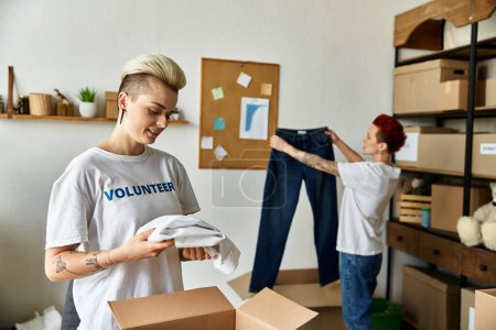 Una joven pareja lesbiana con camisetas voluntarias desempacando ropa en una habitación, trabajando juntos por una causa benéfica.