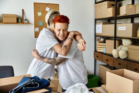Two women with volunteer t-shirts hugging in a room full of boxes, symbolizing compassion and unity.
