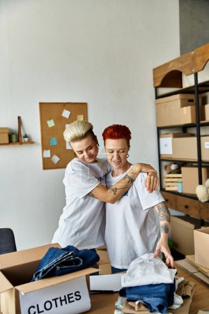 Téléchargez les photos : A young lesbian couple in volunteer t-shirts are standing together in a room, engaged in charity work. - en image libre de droit