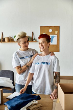 Dos mujeres con camisetas voluntarias de pie unidas en una habitación, trabajando juntas por una causa en la que creen.