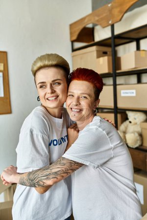 Photo for A woman lovingly hugs another in a room, both wearing volunteer t-shirts. A heartwarming moment of connection. - Royalty Free Image