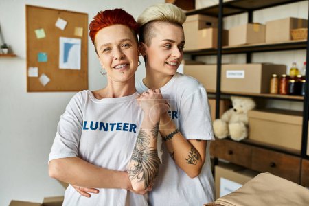 Una joven pareja lesbiana, vistiendo camisetas voluntarias, se mantienen unidas mientras hacen trabajo de caridad.