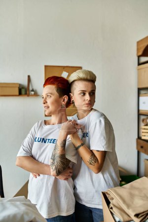 Téléchargez les photos : A young lesbian couple in volunteer t-shirts stands side by side in a room filled with warmth and compassion. - en image libre de droit