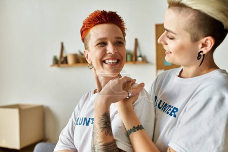 Una joven pareja lesbiana en camisetas voluntarias haciendo trabajo de caridad, de pie uno al lado del otro.