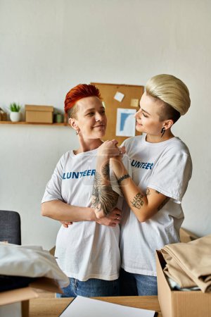 Ein Paar Frauen, Teil der LGBTQ-Community, in freiwilligen T-Shirts, die nebeneinander stehen und Wohltätigkeitsarbeit leisten.