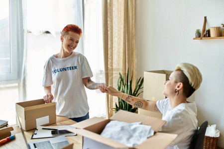 A young woman in a volunteer t-shirt hands a box to her partner, both engaging in a charitable act together.
