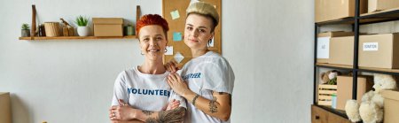 Photo for Young lesbian couple in volunteer t-shirts working on a charity project side by side in a room. - Royalty Free Image