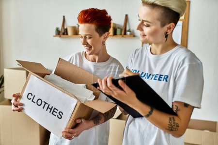 Joven pareja lesbiana en camisetas voluntarias recoge cajas de donaciones para obras de caridad.