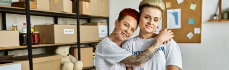 Ein junges lesbisches Paar in freiwilligen Hemden, das sich herzlich umarmt und Liebe und Einheit zeigt, während es karitative Arbeit leistet.