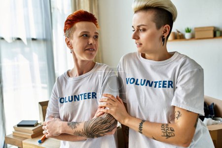 Téléchargez les photos : Un jeune couple de lesbiennes, portant des t-shirts bénévoles, se tient côte à côte, s'engageant activement dans un travail de charité. - en image libre de droit