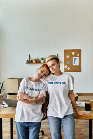 Junge lesbische Paare in freiwilligen T-Shirts stehen in einem Raum, vereint in karitativer Arbeit für die LGBTQ-Community.