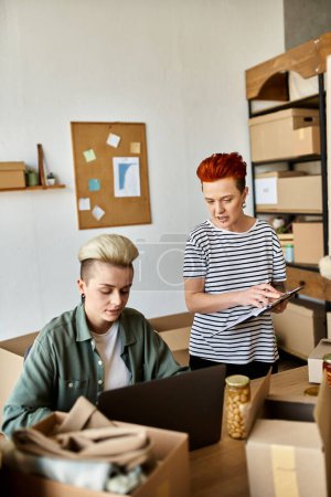 A young lesbian couple, sits at a table in a room filled with boxes.