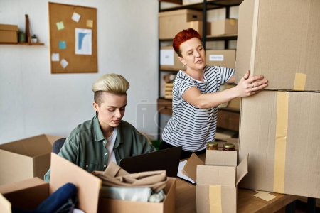 A young lesbian couple work together, moving boxes in a room with focused determination.