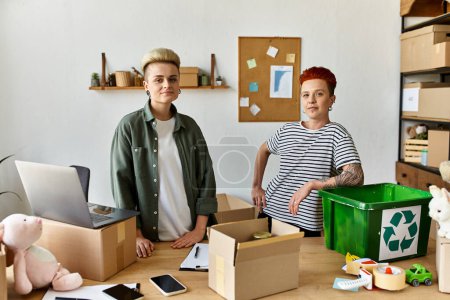 Joven pareja lesbiana está junto a una mesa llena de cajas, trabajando juntos por una causa benéfica.