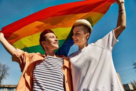 Dos jóvenes alzan orgullosamente una bandera arcoíris en solidaridad con la comunidad LGBTQ, simbolizando el amor y el orgullo.