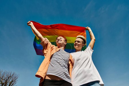 Un jeune couple de lesbiennes tenant joyeusement un drapeau arc-en-ciel à l'extérieur, exprimant amour et fierté envers la communauté LGBTQ.