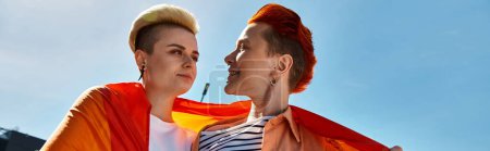 Paar, Teil der LGBTQ-Community, steht stolz mit Regenbogenfahne zusammen.