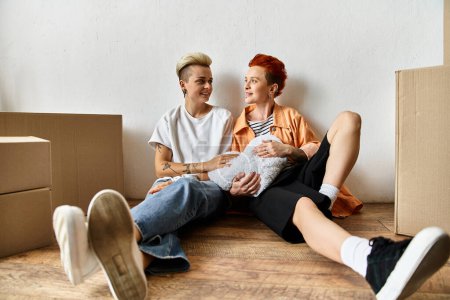 Téléchargez les photos : Un jeune couple lesbien, assis par terre dans un centre de bénévolat près de boîtes, travaillant sur des projets caritatifs. - en image libre de droit