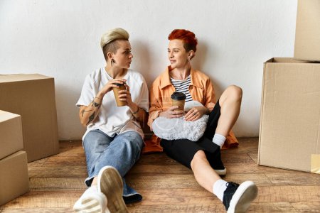 A young lesbian couple sits on the ground near boxes, smiling and enjoying each others company at a volunteer center.