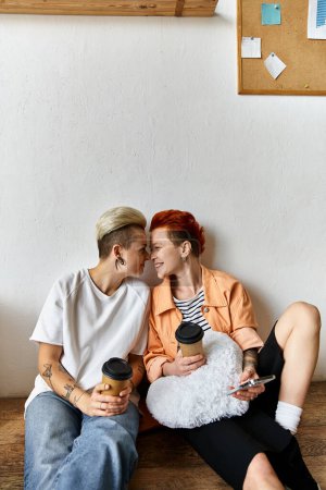 A young lesbian couple taking a break on top of a wooden bench in a volunteer center surrounded by boxes.