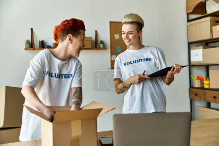 A young lesbian couple in volunteer t-shirts working together in a room, spreading love and kindness through charity.