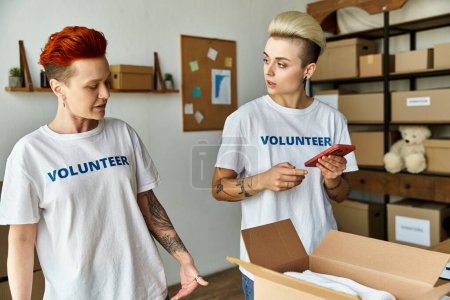 Foto de Una joven pareja de lesbianas, ambas con camisetas voluntarias, se mantienen juntas, unidas en sus esfuerzos por el trabajo de caridad. - Imagen libre de derechos