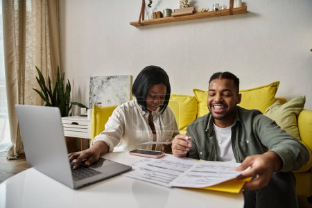 An African American couple sits at a table together, looking at paperwork and smiling.