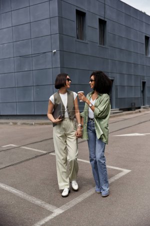 Two women walk and talk outside a building.
