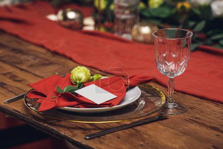 Foto de Blank invitation card, invitation mockup. Wooden table setting with red napkin, flowers, glass plate with golden border. - Imagen libre de derechos
