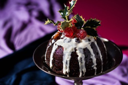Traditional festive Christmas fruit pudding dessert, decorated with cherries and leaves, set in a classic warm red, blue and purple background