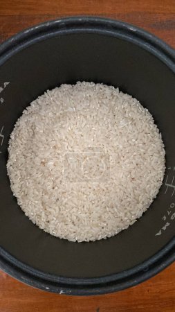 Reis in einer Schüssel mit Maßstab auf einem Holztisch; geeignet für Foodblogs, Ernährungsartikel oder Kochzeitschriften.