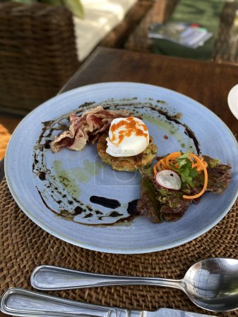 Un petit-déjeuner gastronomique composé d'un ?uf poché sur un lard croustillant brun-haché et garni de légumes frais et de glaçure balsamique.