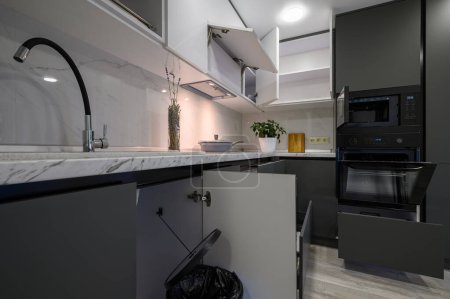 Téléchargez les photos : Showcase interior of modern simple dark grey and white kitchen, drawers retracted, doors open - en image libre de droit