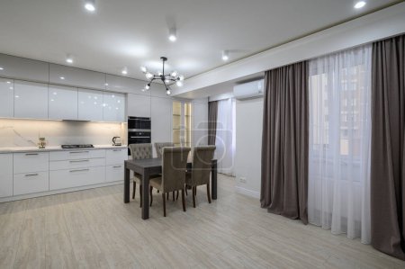 Gran moderno nuevo interior de cocina blanca bien diseñado después de la renovación en el apartamento estudio, ventanas panorámicas cubiertas con cortinas, un montón de espacio de copia