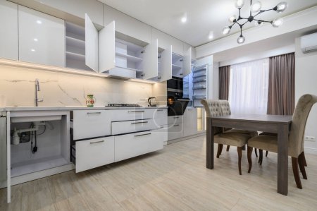 Blanco moderno nuevo interior de cocina blanca bien diseñado después de la renovación en el apartamento estudio, ventanas cubiertas con cortinas