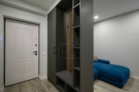 Téléchargez les photos : Hall d'entrée attaché à un petit salon moderne avec grand canapé confortable bleu derrière la garde-robe - en image libre de droit