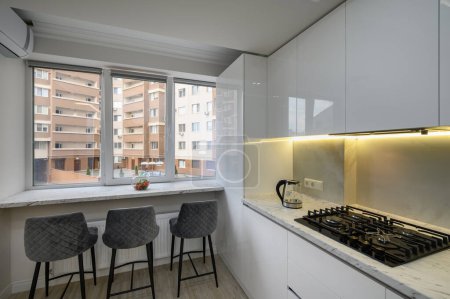 Téléchargez les photos : Cuisine avec cuisinière, chaises près d'une fenêtre, vue sur la ville à l'extérieur de la fenêtre - en image libre de droit