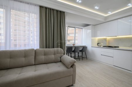 Foto de Sala de estar con un sofá y una cocina en el fondo con una gran ventana y luces en el techo en el interior del apartamento estudio - Imagen libre de derechos