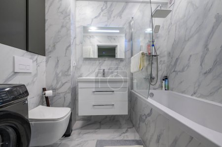 Photo for Modern white marble bathroom interior with toilet seat, washing machine and bathtub - Royalty Free Image