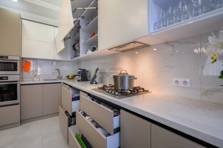 Foto de Moderna cocina de lujo clásica blanca y beige con comedor en el interior del apartamento estudio, algunos cajones están abiertos - Imagen libre de derechos