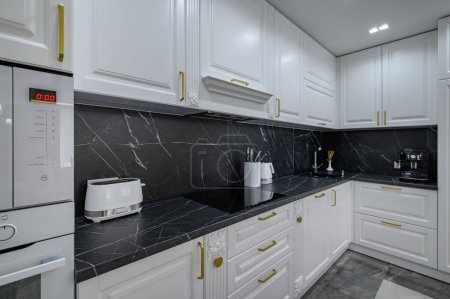 Téléchargez les photos : Grand mobilier de cuisine moderne de luxe blanc avec plan de travail en marbre noir - en image libre de droit