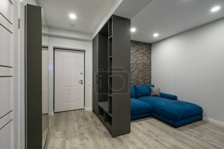 Téléchargez les photos : Hall d'entrée attaché à un petit salon moderne avec grand canapé confortable bleu derrière la garde-robe - en image libre de droit