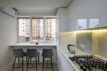 Téléchargez les photos : Cuisine avec cuisinière, chaises près d'une fenêtre, vue sur la ville à l'extérieur de la fenêtre - en image libre de droit
