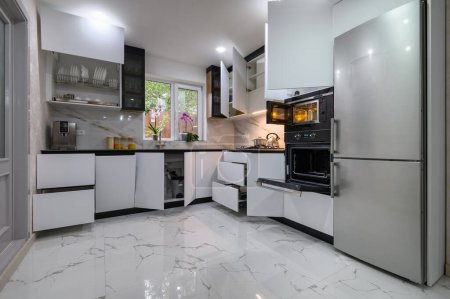 Eine atemberaubende Küche mit weißem, modernem Design, einem luxuriösen Marmorboden und ausziehbaren Regalen für einen einfachen Zugang. Öfen gehen auf.