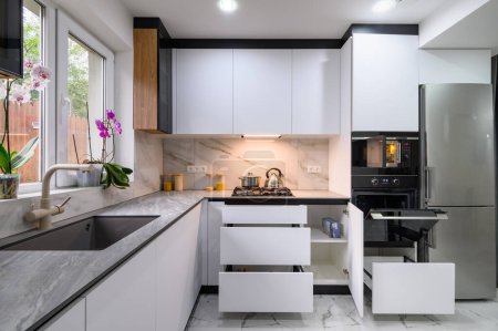Eine helle und luftige Küche mit weißem, modernem Design, einem luxuriösen Marmorboden, einer offenen Ofentür und ausziehbaren Regalen für einfachen Zugang zu Zutaten und Geräten
