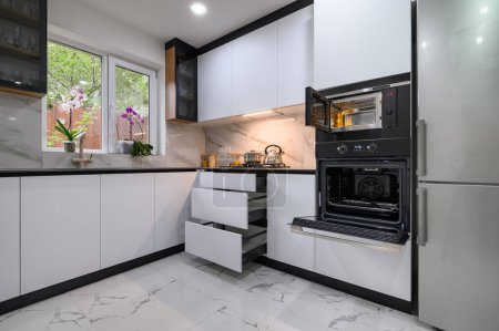 Eine schöne Küche mit weißem und marmorfarbenem Design, einem Marmorboden, einer offenen Ofentür und ausziehbaren Regalen für einfachen Zugang zu Zutaten und Geräten
