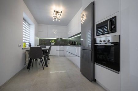 Foto de Luxurious modern trendy white and grey kitchen interior after renovation, with granite counter top and marble floor, dining table next to window - Imagen libre de derechos