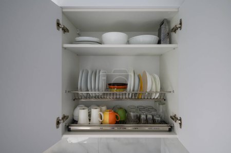 Téléchargez les photos : Grande armoire de cuisine blanche ouverte avec vaisselle, bols, tasses et verres, beaucoup d'espace pour copier - en image libre de droit