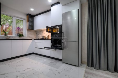 Eine moderne und funktionale Küche mit weißem Design, Marmorboden, grauem Vorhang und offener Ofentür. Perfekt zum Kochen und Leben genießen.